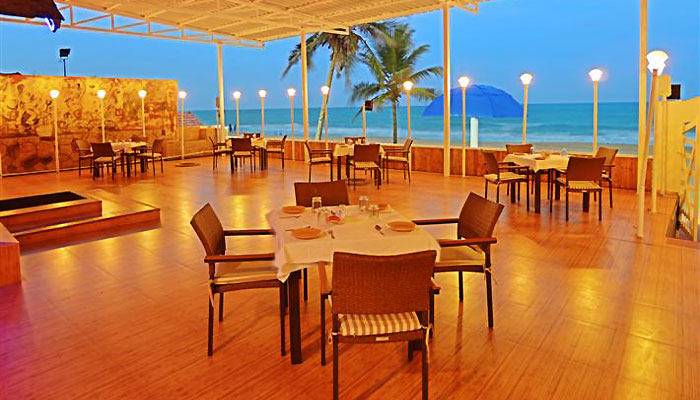 Dining tables and chairs arranged in the beach restaurant with a view of the beach and sea, which extends to the horizon, in Bluebay Beach Resort, ECR, Chennai, near Mahabalipuram